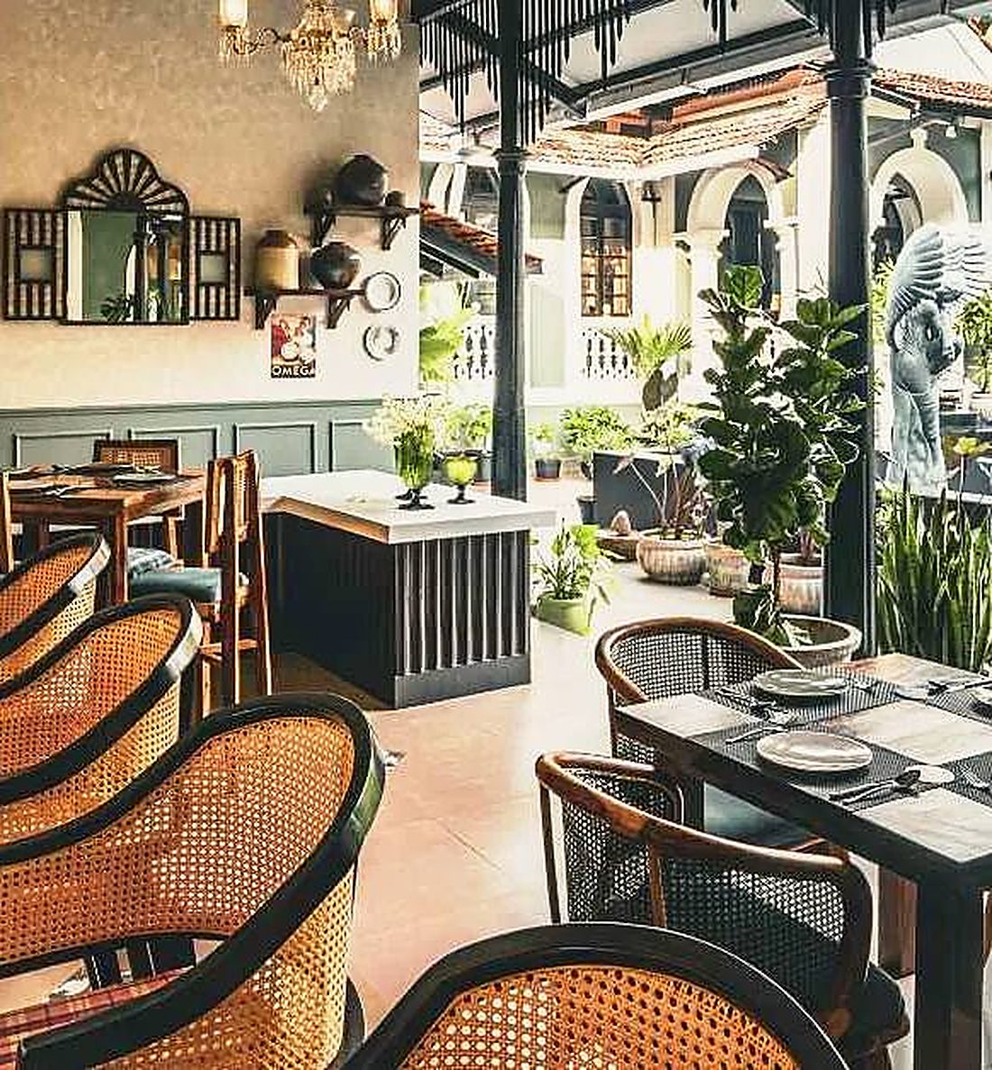 Tables set around a courtyard among plants, cane chairs in the foreground