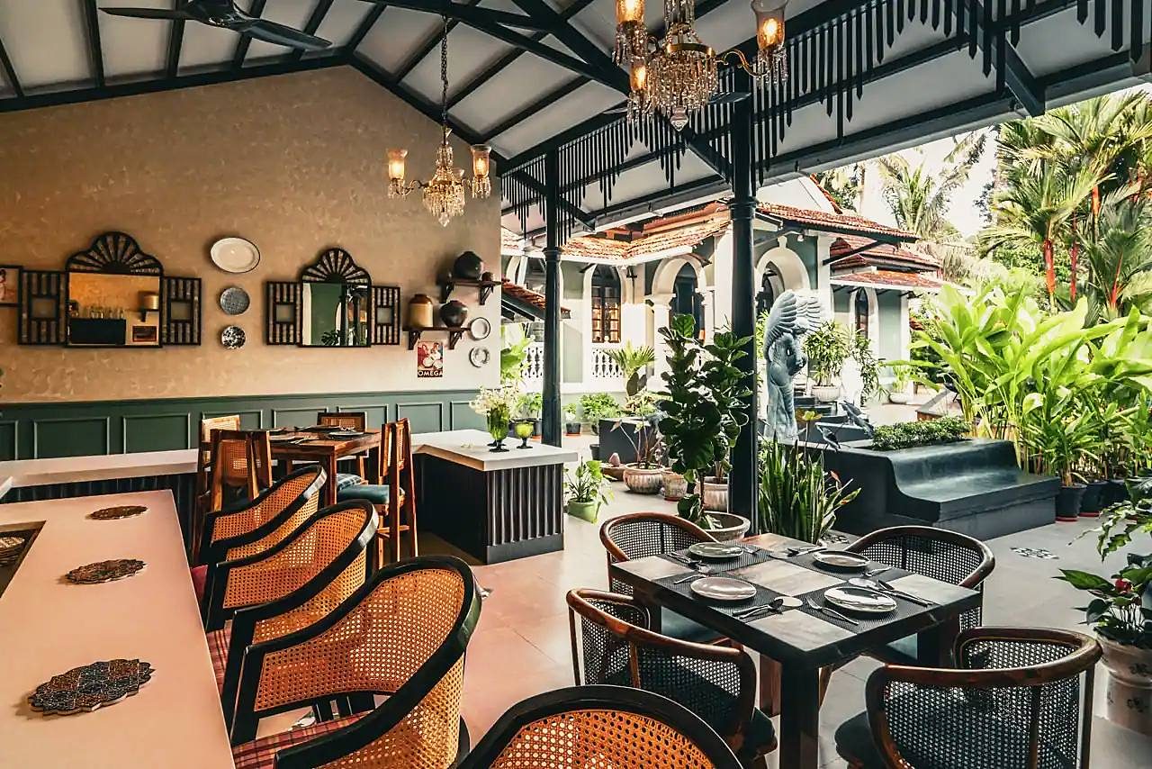 A covered verandah with cane chairs and set tables, open to a garden